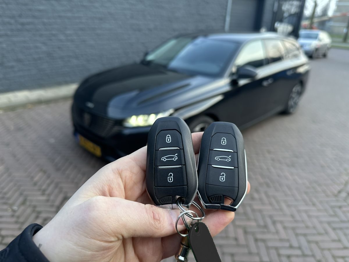 Twee nieuwe smart keys voor een Peugeot 508, bijgemaakt in Enschede, met de auto op de achtergrond